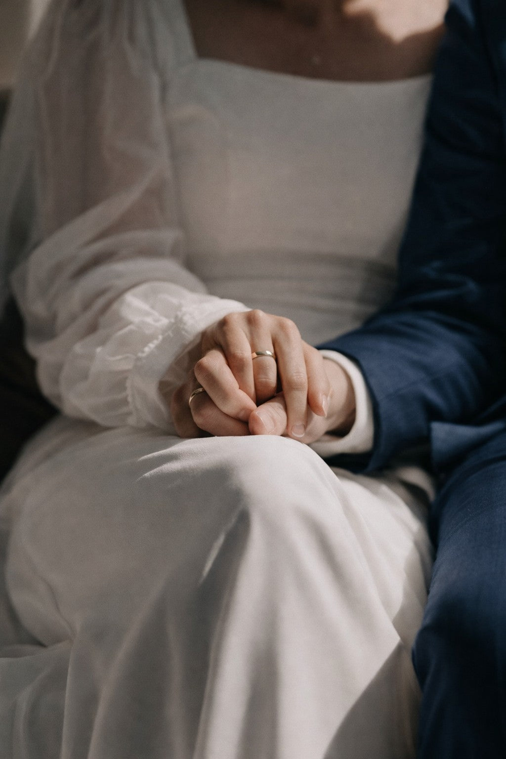 Manos de una pareja sentada, entrelazadas, con alianzas de boda minimalistas en oro fabricadas artesanalmente.